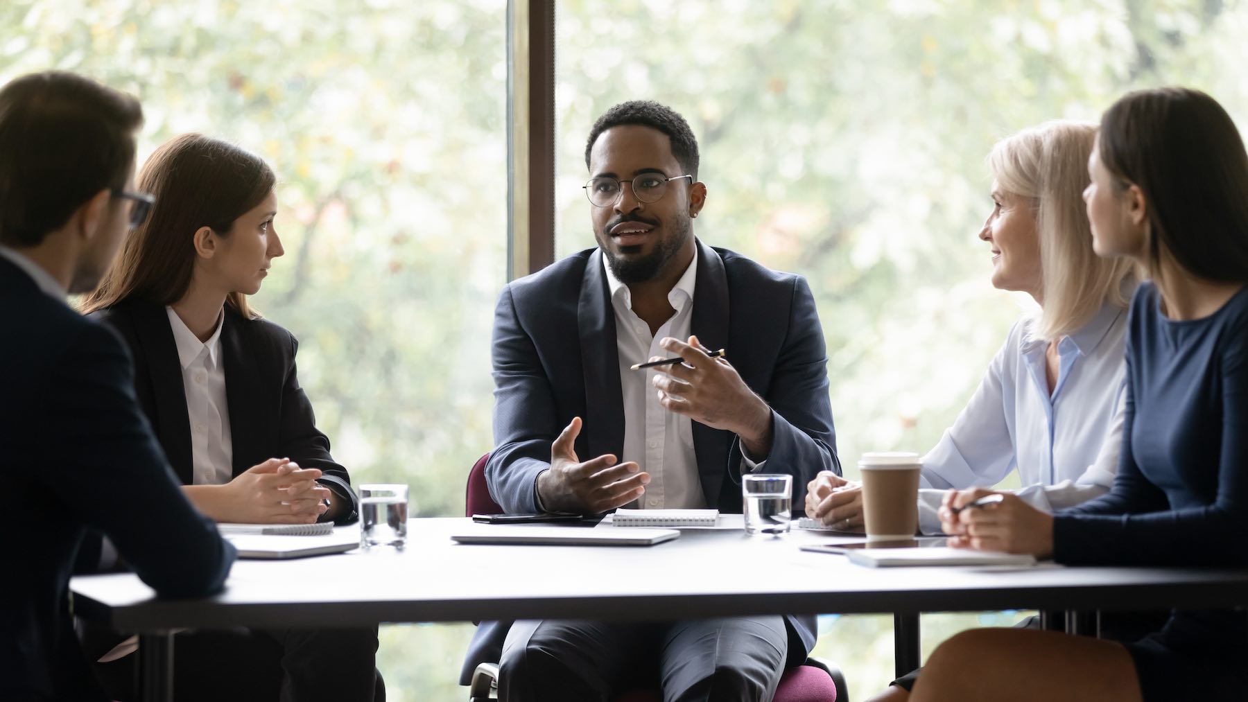 Engaged, motivated business leader talking to team, meeting with employees, managers. Corporate coach, mentor training staff. Diverse group discussing work project at table