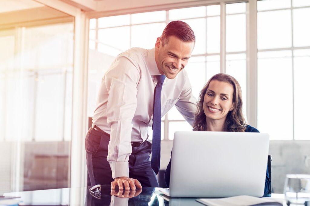 Young business woman showing information on laptop to businessman. Businesswoman explaining plan to businessman on computer. Colleagues working together in modern office.