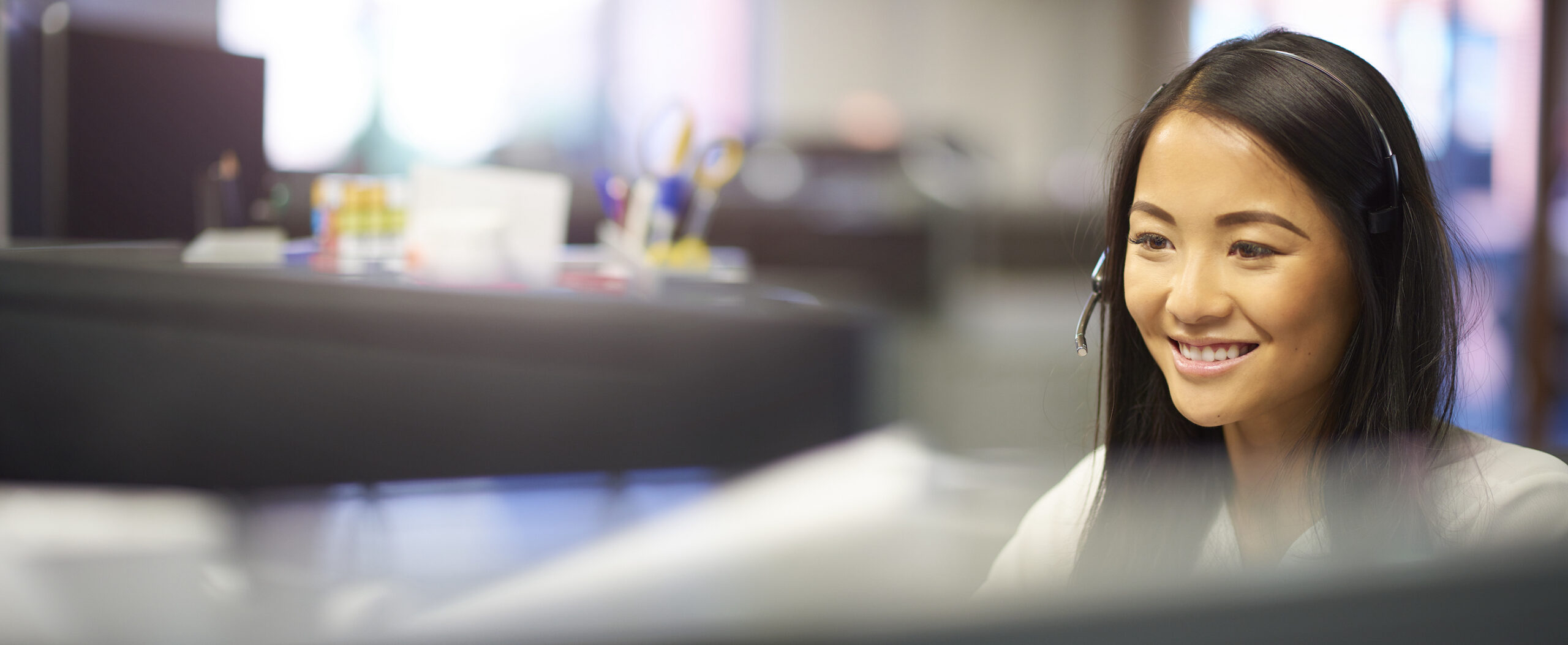 A young office worker is chatting happily on the phone in a large open plan office.